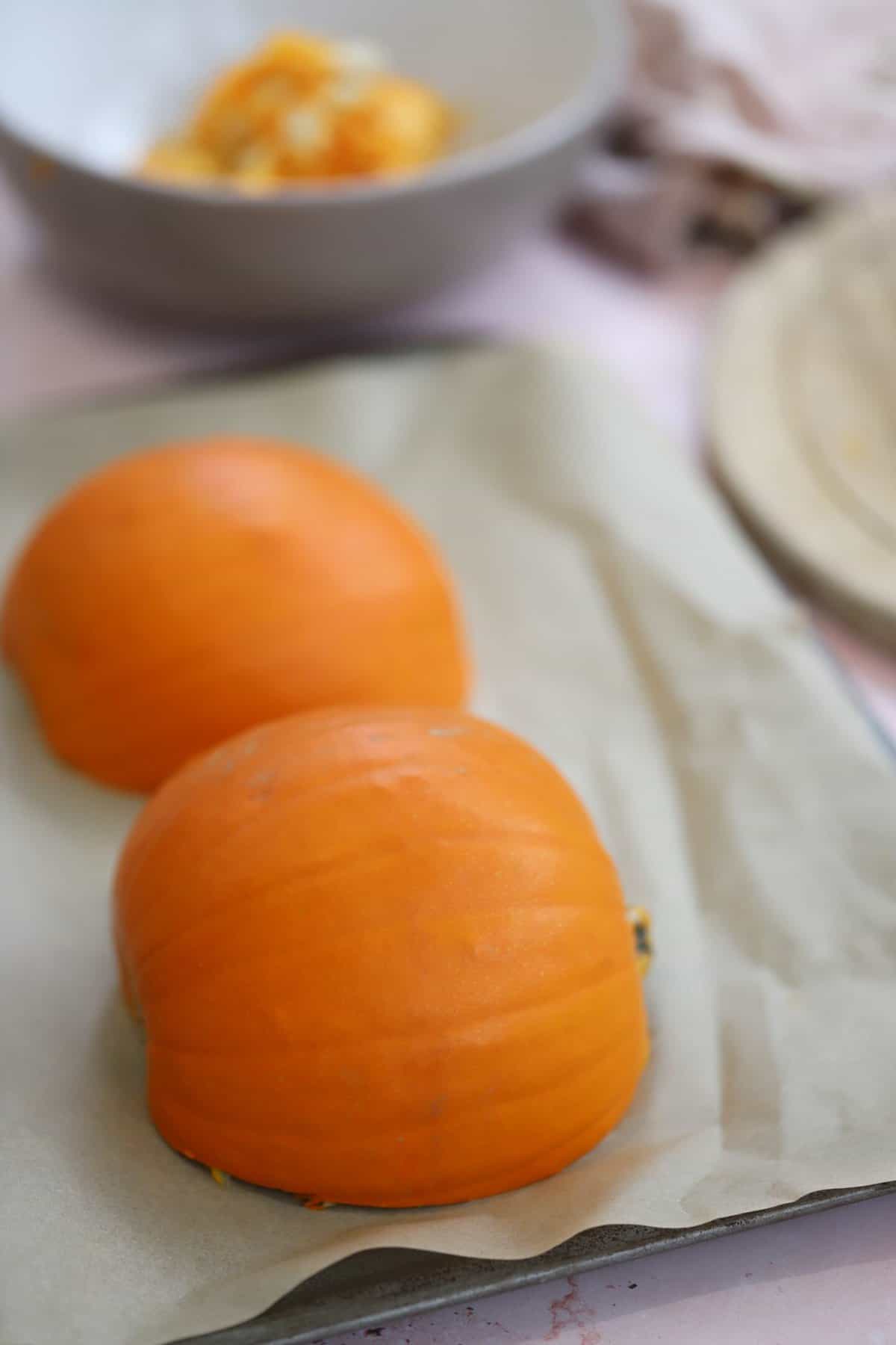 Two pumpkin halves face down on a baking tray ready to go in the oven.